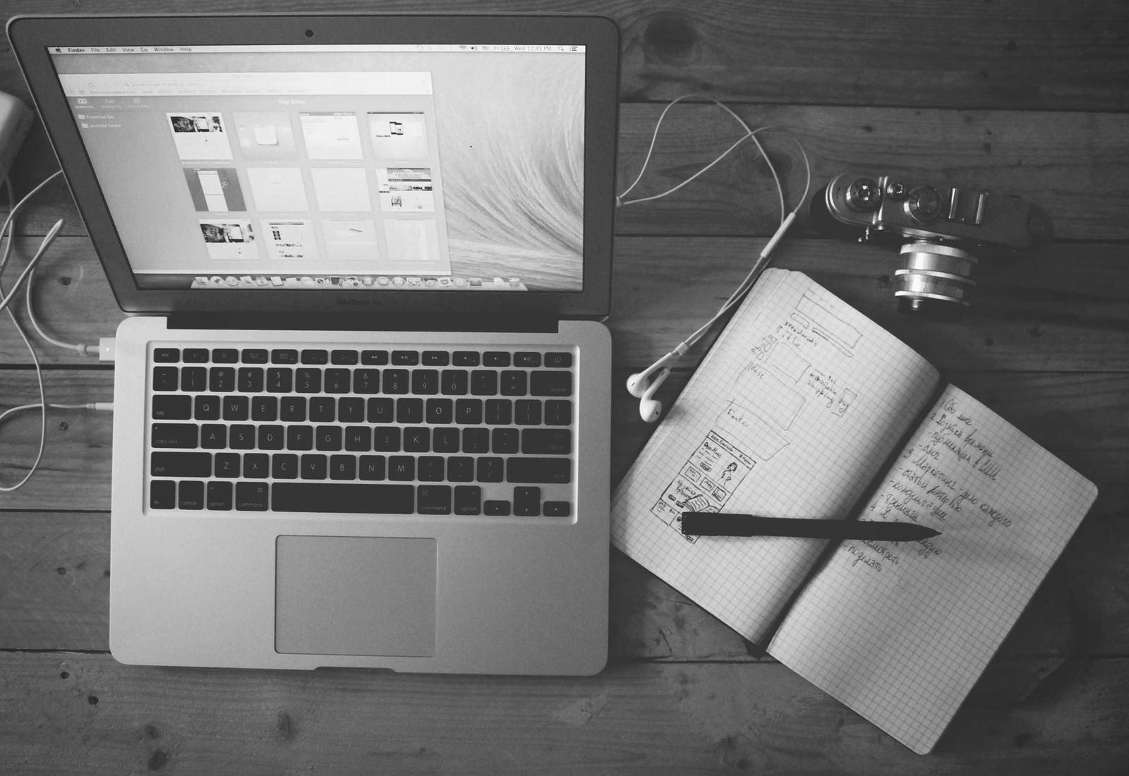 Laptop beside an open notebook of hand-drawn interface sketches